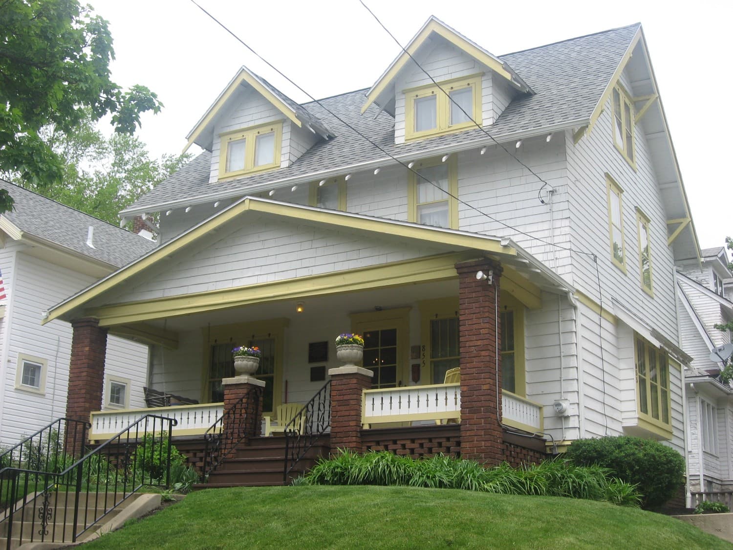 A white clapboard house with a wide front porch, brick pillars and a lawn, photographed from the street.