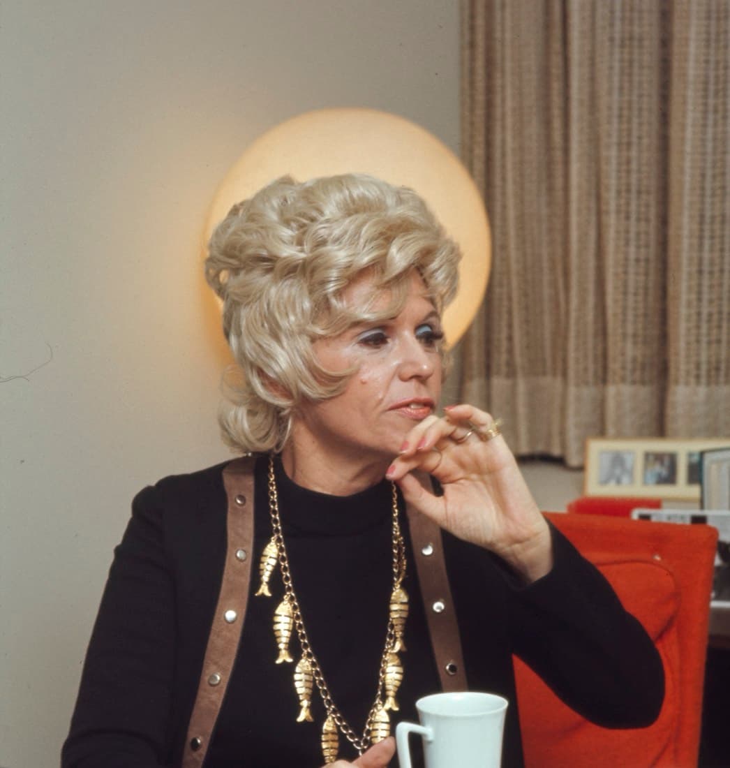 A colour portrait of Jean Nidetch seated, resting her chin on her hand, wearing a fish-link necklace.
